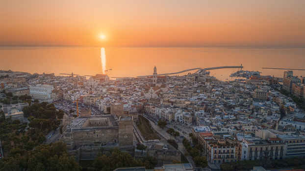 Aerial view of the historic old town featuring the Castello Svevo and the Basilica of Saint Nicholas illuminated by the warm glow of sunset in Bari Apulia Italy.