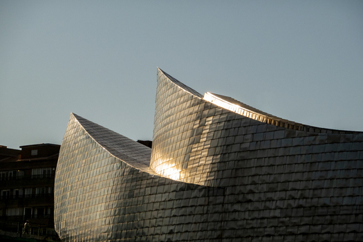 View of the shimmering titanium panels and curved architectural lines of the Guggenheim Museum Bilbao under a clear sky in Bilbao Euskadi Spain. View of the shimmering titanium panels and curved architectural lines of the Guggenheim Museum Bilbao under a clear sky in Bilbao Euskadi Spain.