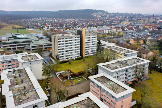 Aerial view of residential apartment blocks and suburban houses surrounded by green spaces and distant hills under an overcast sky in Forchheim Bavaria Germany.