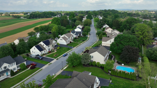 Aerial view of a suburban neighborhood featuring single family homes with green lawns a swimming pool solar panels on rooftops and surrounding farmland in Leola Pennsylvania United States. Aerial view of a suburban neighborhood featuring single family homes with green lawns a swimming pool solar panels on rooftops and surrounding farmland in Leola Pennsylvania United States.