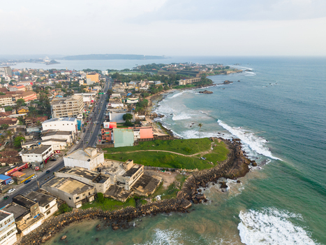 Aerial view of the coastal city skyline and rocky shoreline with waves crashing against the green headland in Galle Southern Province Sri Lanka.