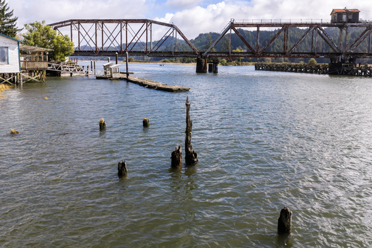 Aerial view of the historic Siuslaw River Train Bridge spanning the water with wooden pilings in the foreground and lush trees along the banks in Florence Oregon United States.
