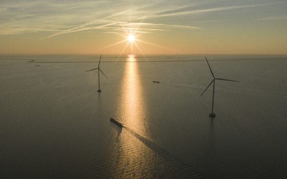 Aerial view of offshore wind turbines and a cargo ship on the calm sea during a golden sunset Netherlands. Aerial view of offshore wind turbines and a cargo ship on the calm sea during a golden sunset Netherlands.