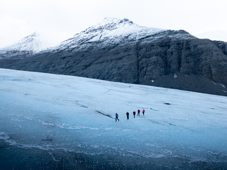 Aerial view of a group of hikers trekking across the blue ice of Breidamerkurjokull glacier with snow capped mountains in the background in Sveitarfelagid Hornafjordur Iceland. Aerial view of a group of hikers trekking across the blue ice of Breidamerkurjokull glacier with snow capped mountains in the background in Sveitarfelagid Hornafjordur Iceland.
