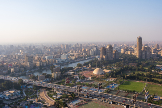 View of a sprawling cityscape with modern buildings and a flowing river under a hazy sky captured from an aerial perspective Zamalek Cairo Governorate Egypt. View of a sprawling cityscape with modern buildings and a flowing river under a hazy sky captured from an aerial perspective Zamalek Cairo Governorate Egypt.