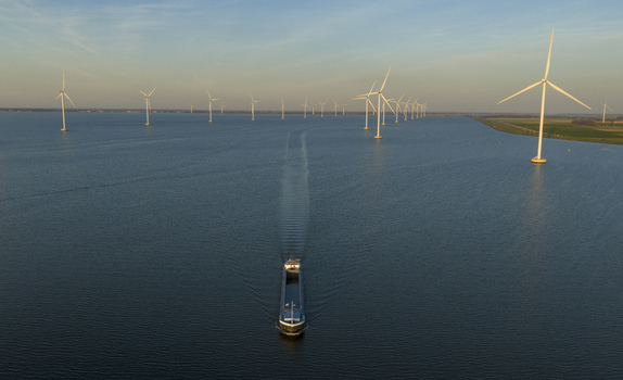 Aerial view of a large cargo ship sailing through an offshore wind farm with rows of turbines under a clear golden hour sky in Netherlands. Aerial view of a large cargo ship sailing through an offshore wind farm with rows of turbines under a clear golden hour sky in Netherlands.