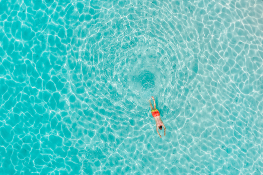 Aerial view of a person swimming in crystal clear turquoise water with sunlight reflecting on the surface in Innafinolhu Haa Alif Atoll Maldives. Aerial view of a person swimming in crystal clear turquoise water with sunlight reflecting on the surface in Innafinolhu Haa Alif Atoll Maldives.