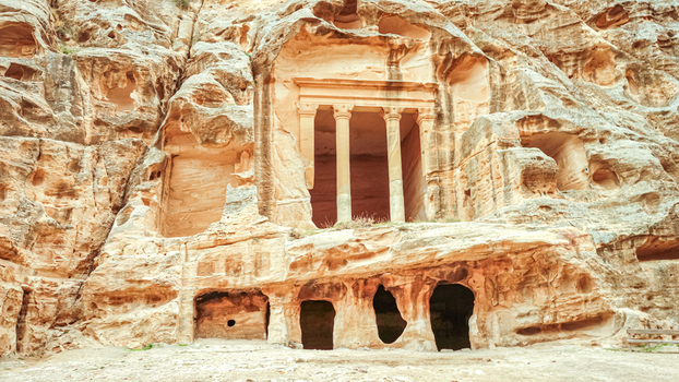 View of an ancient Nabataean rock cut tomb facade featuring carved columns and weathered sandstone cliffs in Wadi Musa Ma an Governorate Jordan. View of an ancient Nabataean rock cut tomb facade featuring carved columns and weathered sandstone cliffs in Wadi Musa Ma an Governorate Jordan.