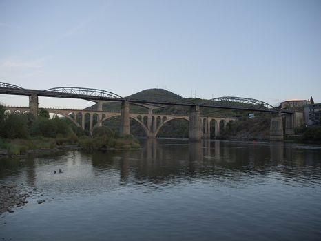 View of the historic bridge spanning the Douro River in Peso da Regua with rolling hills and calm water under a clear sky in Peso da Regua Vila Real District Portugal.