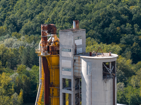 Aerial view of the Sacci S.P.A. cement factory featuring tall concrete silos and yellow industrial pipes set against dense green forest in Castelraimondo Marche Italy. Aerial view of the Sacci S.P.A. cement factory featuring tall concrete silos and yellow industrial pipes set against dense green forest in Castelraimondo Marche Italy.