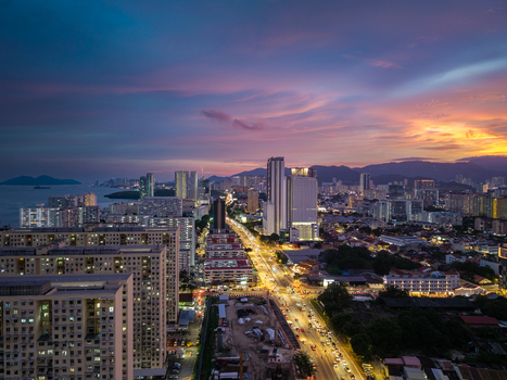 George Town Malaysia 22 September 2026 Aerial view of the George Town cityscape at twilight with illuminated streets high rise buildings and a vibrant sunset sky over the coastline.