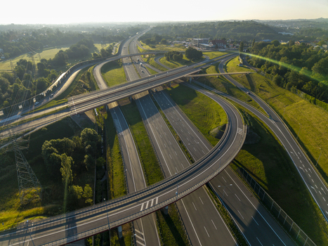 Aerial view of a complex highway interchange with multiple lanes and curved overpasses surrounded by green fields and trees during golden hour Krakow Lesser Poland Voivode Poland.