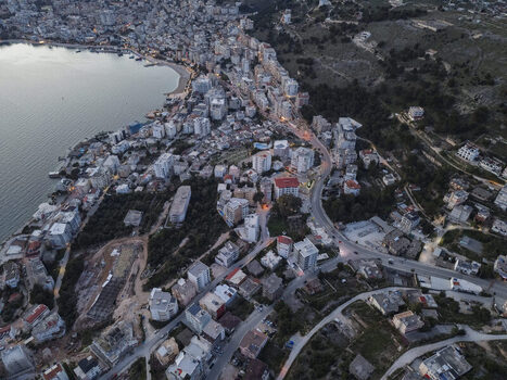 Aerial view of the coastal city with dense urban buildings winding roads and the calm bay at twilight in Saranda Vlore County Albania. Aerial view of the coastal city with dense urban buildings winding roads and the calm bay at twilight in Saranda Vlore County Albania.