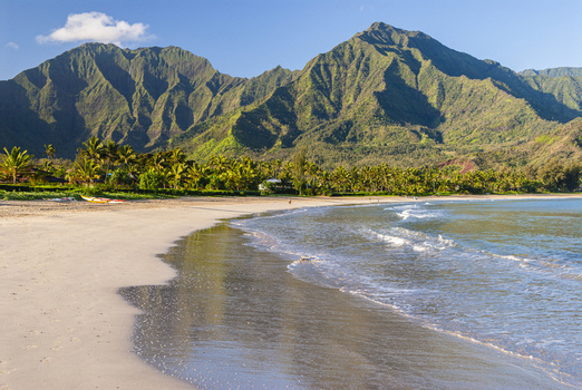 View of Hanalei Bay with its pristine sandy beach lush green mountains in the background and gentle waves rolling onto the shore in Hanalei Hawaii United States. View of Hanalei Bay with its pristine sandy beach lush green mountains in the background and gentle waves rolling onto the shore in Hanalei Hawaii United States.