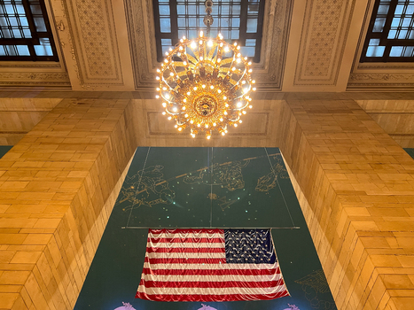 View of Grand Central Terminal interior featuring the American flag a celestial ceiling mural and a glowing chandelier New York New York United States. View of Grand Central Terminal interior featuring the American flag a celestial ceiling mural and a glowing chandelier New York New York United States.