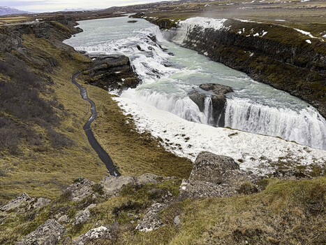 View of Gullfoss waterfall cascading into the Hvita River canyon with rocky terrain and patches of snow in Gullfoss Iceland. View of Gullfoss waterfall cascading into the Hvita River canyon with rocky terrain and patches of snow in Gullfoss Iceland.