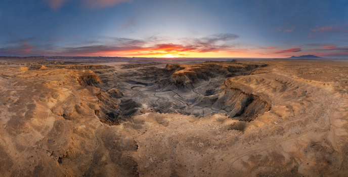 Aerial view of the rugged badlands landscape with deep canyons and eroded rock formations under a dramatic sunset sky in Hanksville Utah United States.