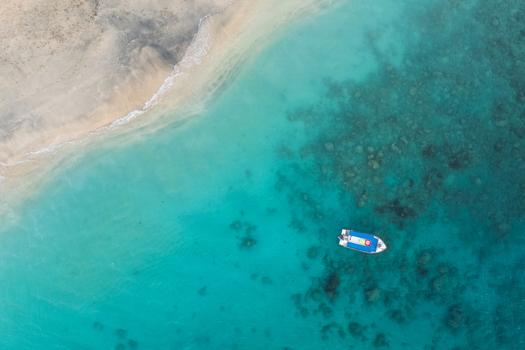 Aerial view of Tanjung Aan Beach with a small boat floating on turquoise water over coral reefs in Kecamatan Pujut Nusa Tenggara Barat Indonesia.