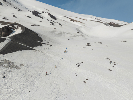 Aerial view of the south side of Mount Etna with a line of hikers trekking across the snowy volcanic landscape under a clear blue sky Nicolosi Sicilia Italy. Aerial view of the south side of Mount Etna with a line of hikers trekking across the snowy volcanic landscape under a clear blue sky Nicolosi Sicilia Italy.