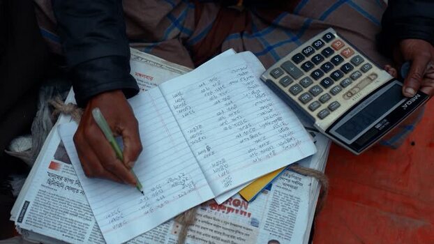 View of a person writing in a notebook with a calculator Bangladesh. View of a person writing in a notebook with a calculator Bangladesh.