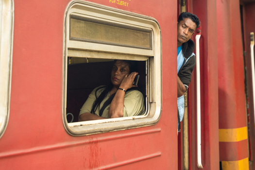 Sri Lanka 06 February 2026 View of passengers on a red train with a woman looking out of the window and a man leaning from the doorway.