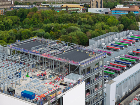 Aerial view of a large data center construction site featuring steel framework colorful cooling units and surrounding greenery in the United Kingdom.