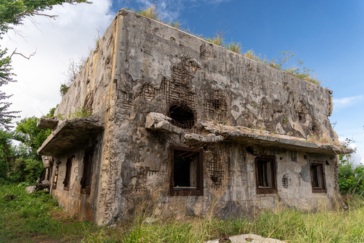 View of the historic North Field Base a weathered concrete structure with exposed rebar and overgrown vegetation under a blue sky in Northern Tinian Tinian Northern Mariana Islands. View of the historic North Field Base a weathered concrete structure with exposed rebar and overgrown vegetation under a blue sky in Northern Tinian Tinian Northern Mariana Islands.