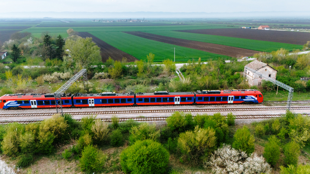 Aerial view of a vibrant red and blue train cutting through the lush green landscape a testament to modern transport amidst nature s serenity Sremska Mitrovica Vojvodina Serbia. Aerial view of a vibrant red and blue train cutting through the lush green landscape a testament to modern transport amidst nature s serenity Sremska Mitrovica Vojvodina Serbia.
