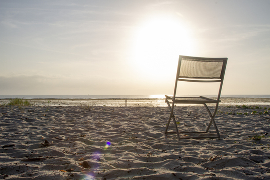 View of Tiwi Beach with a lone folding chair on the sandy shore facing the bright sun over the ocean horizon at sunrise Tiwi Wilaya ya Kwale Kenya. View of Tiwi Beach with a lone folding chair on the sandy shore facing the bright sun over the ocean horizon at sunrise Tiwi Wilaya ya Kwale Kenya.