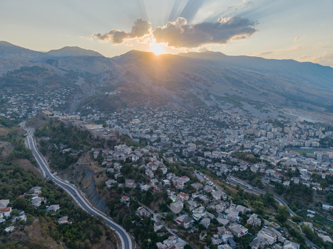Aerial view of Gjirokaster Castle perched on a hillside overlooking the historic stone city with winding roads and mountains under a sunset sky in Gjirokaster Gjirokaster County Albania. Aerial view of Gjirokaster Castle perched on a hillside overlooking the historic stone city with winding roads and mountains under a sunset sky in Gjirokaster Gjirokaster County Albania.