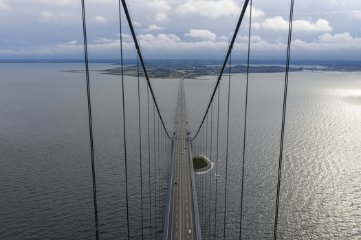 Aerial view of the Great Belt Bridge with its massive suspension cables stretching over the sea towards the horizon under a cloudy sky Denmark. Aerial view of the Great Belt Bridge with its massive suspension cables stretching over the sea towards the horizon under a cloudy sky Denmark.