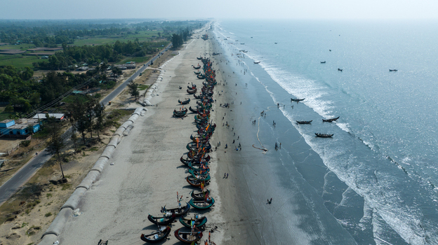 Aerial view of fishing boats resting on the sandy beach with the turquoise sea contrasting against the lush green landscape Cox s Bazar Chittagong Division Bangladesh. Aerial view of fishing boats resting on the sandy beach with the turquoise sea contrasting against the lush green landscape Cox s Bazar Chittagong Division Bangladesh.