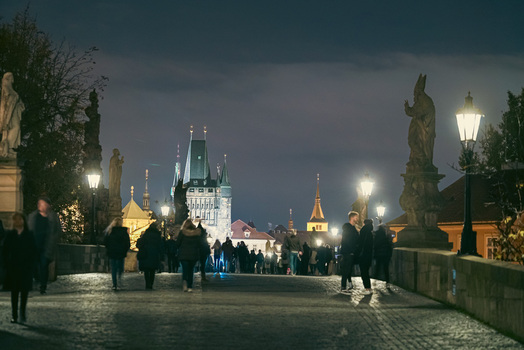 Prague Czechia 03 November 2021 View of Charles Bridge at night with historic statues glowing street lamps and people walking across the stone pavement. Prague Czechia 03 November 2021 View of Charles Bridge at night with historic statues glowing street lamps and people walking across the stone pavement.
