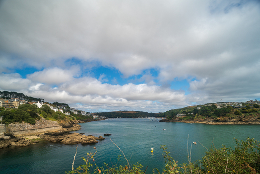 View of the Fowey River with boats moored in the harbour surrounded by the historic town of Fowey and lush green hills under a cloudy sky in Fowey Cornwall United Kingdom. View of the Fowey River with boats moored in the harbour surrounded by the historic town of Fowey and lush green hills under a cloudy sky in Fowey Cornwall United Kingdom.