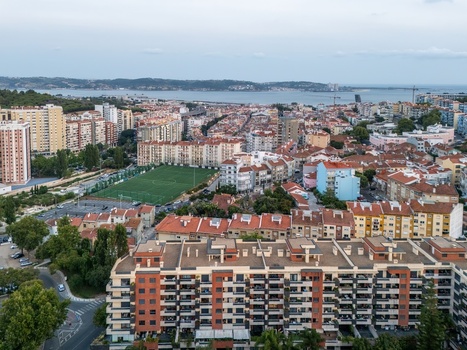 Aerial view of dense residential apartment buildings a green soccer field and urban streets with the Tagus River in the background in Lisbon Lisbon Portugal.