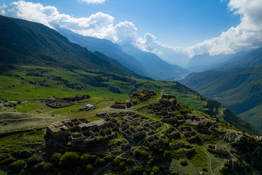 Aerial view of ancient stone ruins perched on a grassy hilltop surrounded by lush green mountain slopes and deep valleys under a bright blue sky in Nepal.