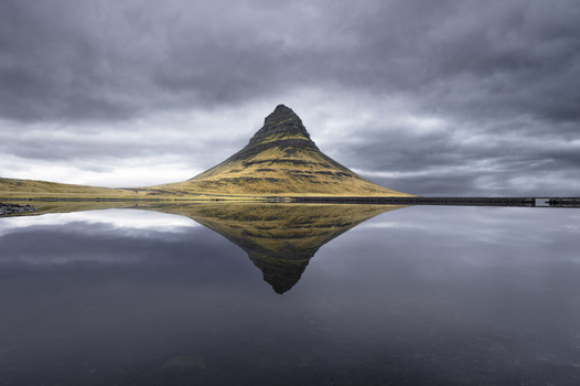 View of Kirkjufell mountain perfectly reflected in the calm surface of a lake under a dramatic overcast sky Kirkjufell Grundarfjardarbaer Iceland.