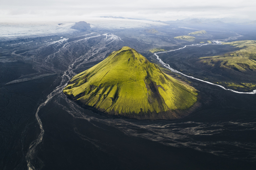 Aerial view of the vibrant mossy green Mælifell volcano rising from the stark black volcanic sands contrasted against the distant glacier Maelifell Iceland. Aerial view of the vibrant mossy green Mælifell volcano rising from the stark black volcanic sands contrasted against the distant glacier Maelifell Iceland.
