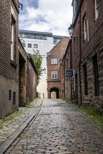 Newcastle upon Tyne United Kingdom 13 July 2026 View of a narrow cobblestone alleyway lined with historic red brick buildings and stone walls under a cloudy sky. Newcastle upon Tyne United Kingdom 13 July 2026 View of a narrow cobblestone alleyway lined with historic red brick buildings and stone walls under a cloudy sky.