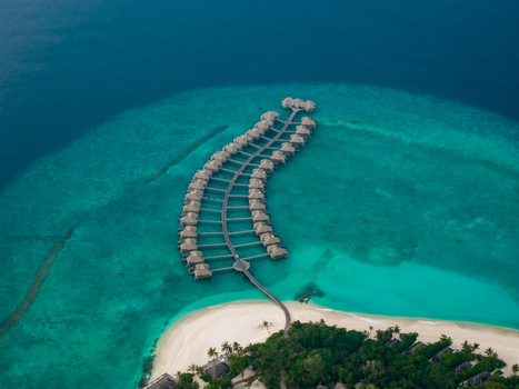 Aerial view of a luxurious overwater resort curving gracefully from a vibrant green island into the sparkling turquoise sea Hoarafushi Thiladhunmathee Uthuruburi Maldives. Aerial view of a luxurious overwater resort curving gracefully from a vibrant green island into the sparkling turquoise sea Hoarafushi Thiladhunmathee Uthuruburi Maldives.
