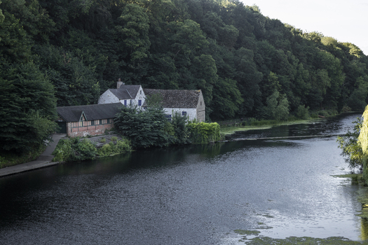 View of a historic stone building nestled on the banks of a calm river surrounded by lush green trees in Durham England United Kingdom. View of a historic stone building nestled on the banks of a calm river surrounded by lush green trees in Durham England United Kingdom.
