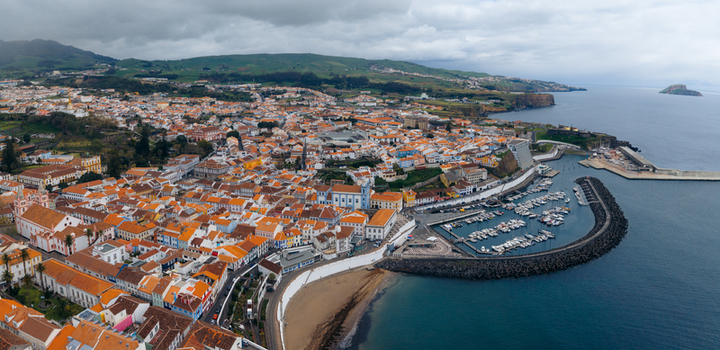 Aerial view of the historic city center with orange tiled rooftops the harbor filled with boats and the Se Cathedral under a cloudy sky in Angra do Heroismo Azores Portugal.