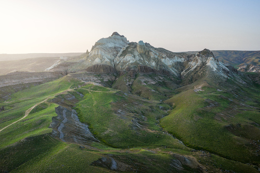 Aerial view of Airakty mountains with lush green slopes rocky peaks and winding dirt paths under a soft morning light in Shetpe Mangystau Region Kazakhstan.