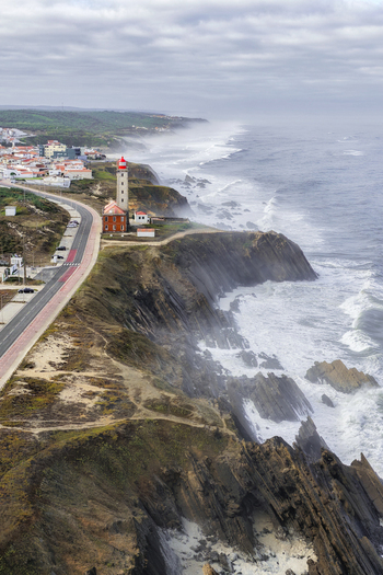 Aerial view of Farol Penedo da Saudade on a rugged cliffside with crashing waves and a coastal road in Marinha Grande Leiria Portugal. Aerial view of Farol Penedo da Saudade on a rugged cliffside with crashing waves and a coastal road in Marinha Grande Leiria Portugal.