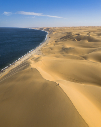 Aerial view of golden sand dunes meeting the deep blue sea under a clear sky creating a striking contrast of colors and textures Anichab Namibia. Aerial view of golden sand dunes meeting the deep blue sea under a clear sky creating a striking contrast of colors and textures Anichab Namibia.