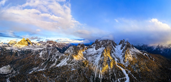 Aerial view of Tre Cime di Lavaredo and Cadini of Misurina in golden sunlight against a backdrop of azure skies and swirling clouds Veneto Italy. Aerial view of Tre Cime di Lavaredo and Cadini of Misurina in golden sunlight against a backdrop of azure skies and swirling clouds Veneto Italy.