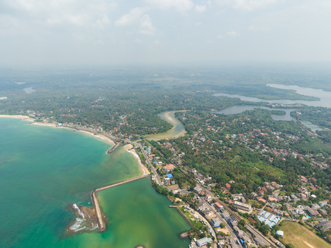 Aerial view of the turquoise coastline with a long breakwater sandy beaches and lush tropical vegetation along the coastal road Hikkaduwa Southern Province Sri Lanka. Aerial view of the turquoise coastline with a long breakwater sandy beaches and lush tropical vegetation along the coastal road Hikkaduwa Southern Province Sri Lanka.