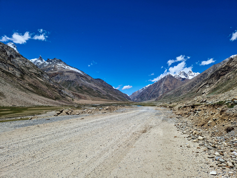 View of the Penzi La road winding through a high altitude mountain valley with snow capped peaks and rocky terrain under a clear blue sky in Zanskar Ladakh India.