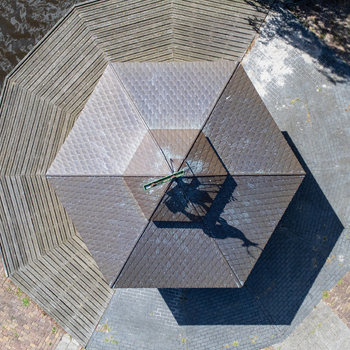 Aerial view of the geometric patterns of a hexagonal structure with brown tiles and a central metal feature casting shadows on the surface Tollebeek Flevoland Netherlands.