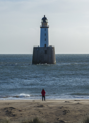 Aerial view of Rattray Head Lighthouse standing in the North Sea with a person in a red jacket on the sandy beach in the foreground in Peterhead Scotland United Kingdom. Aerial view of Rattray Head Lighthouse standing in the North Sea with a person in a red jacket on the sandy beach in the foreground in Peterhead Scotland United Kingdom.